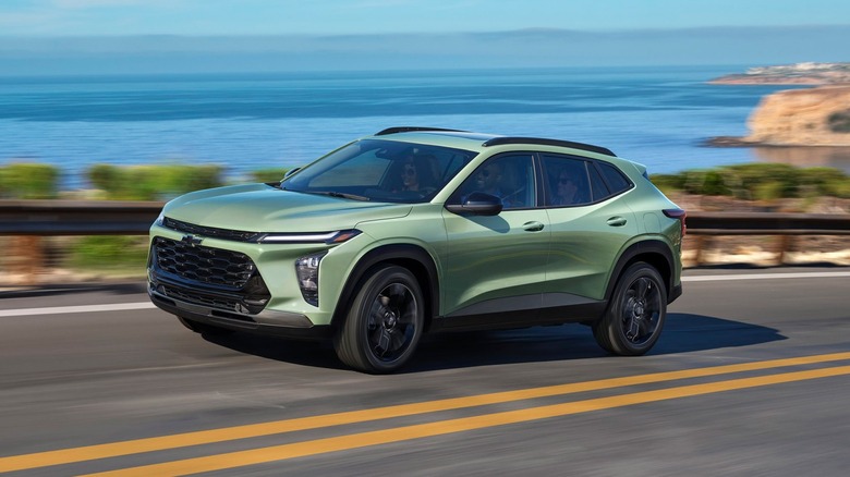 A green 2026 Chevrolet Trax along a coastal highway with ocean views in the background.