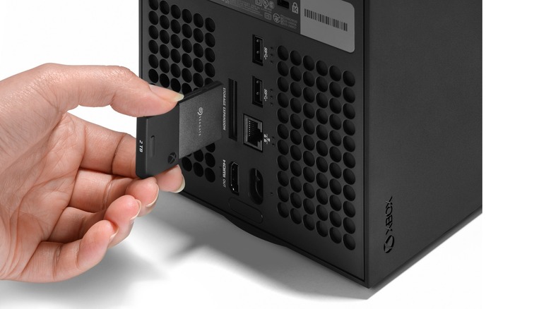 A hand inserts a Seagate storage expansion card into the back of an Xbox.