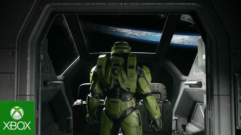 Master Chief stands in a spaceship bay looking out at a Halo ring in space.