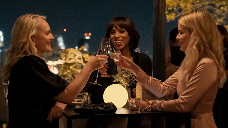 Three women smiling and toasting with champagne glasses at an evening gathering.