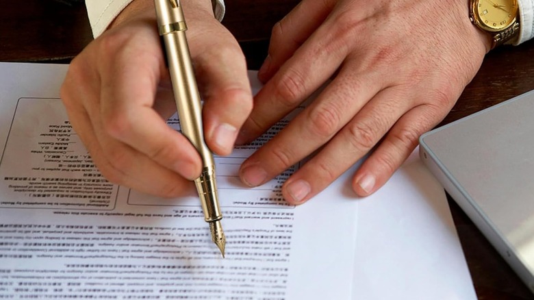 Person in a suit writing on a document with a gold fountain pen.