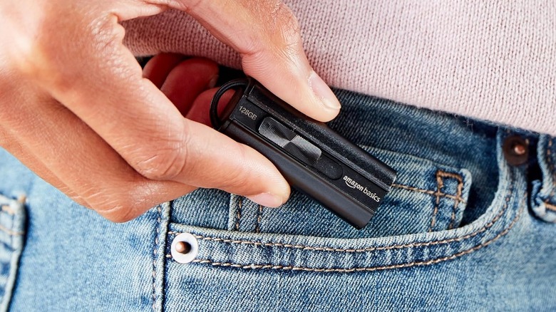 A person sliding a small black flash drive into a blue jeans pocket.