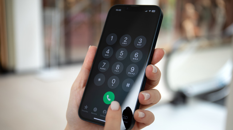 A person holding an iPhone and entering a number into the keypad