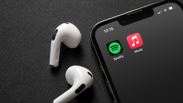 AirPods sitting next to iPhone with Spotify and Apple Music app