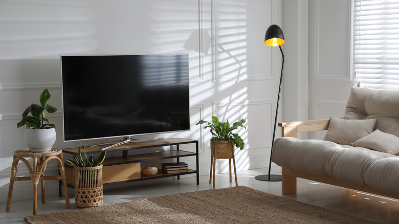 A TV placed in a living room next to a counch and a lamp