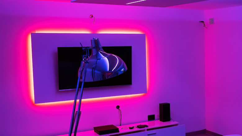 A TV on a wall with LED strips behind it.