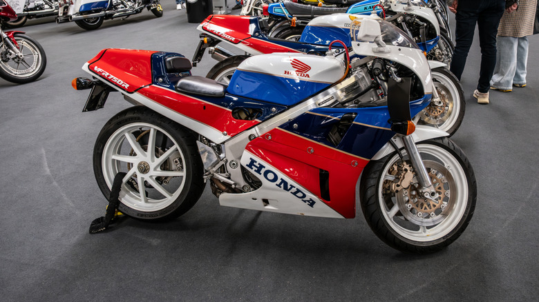 A multicolored Honda VFR750R RC30 finished in white, red, and blue, parked in a bike show.