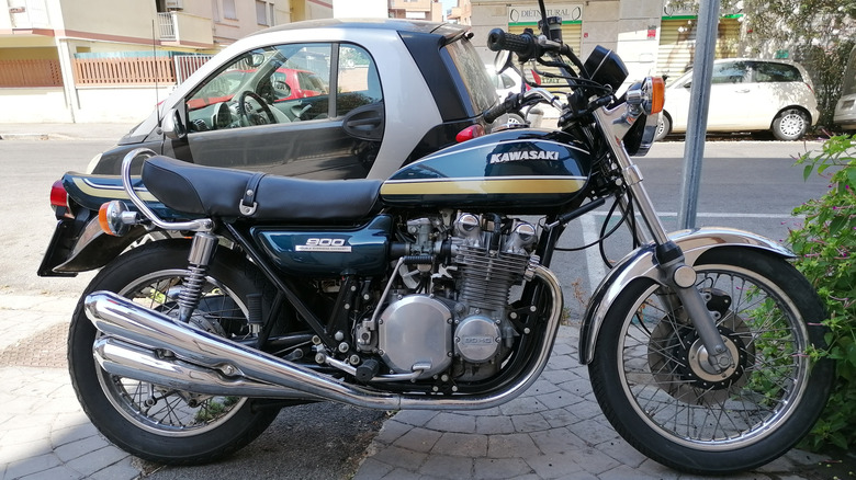 A green and black Kawasaki Z1 900 motorbike parked in front of a beige and pink house.