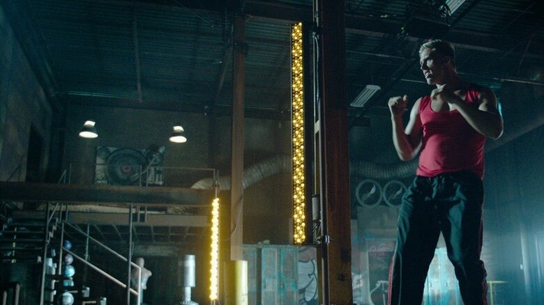 A man in a red tank top shadowboxes in a spacious, industrial gym.