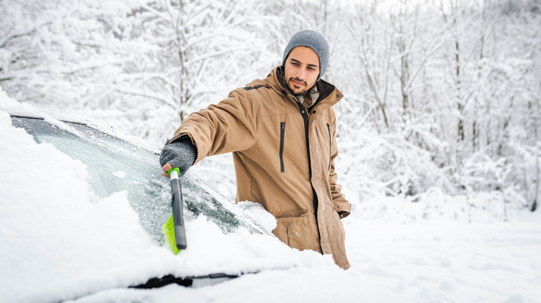 Man brushing snow off of windshield