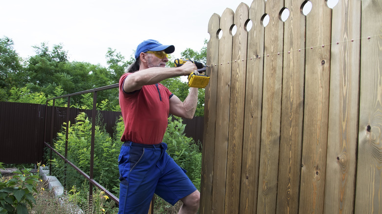 Man using a tool to install a piece of wooden fence