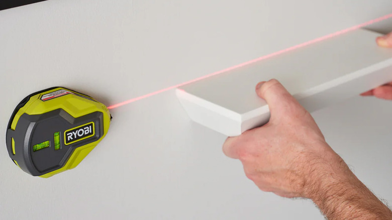 A person hanging a shelf using a laser level