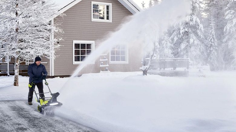 A man using a Ryobi snowblower to clear their driveway