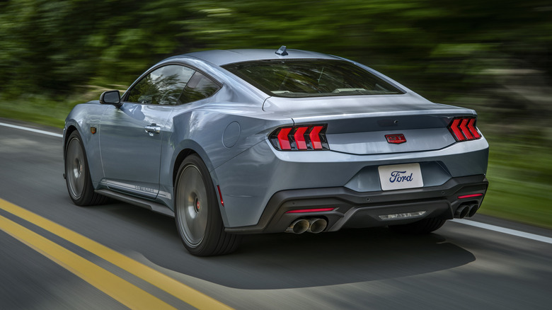 Blue 2025 Ford Mustang GT 60th Anniversary driving on mountain road, rear 3/4 view