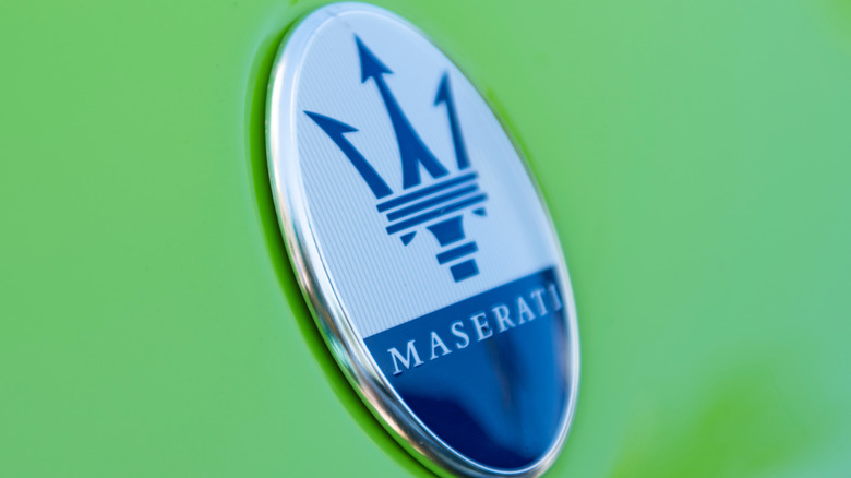 A white and blue Maserati trident badge on the bonnet of a green car.