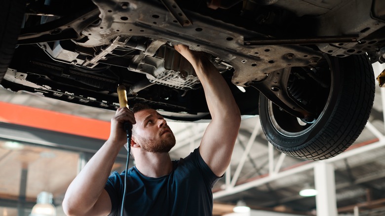 Mechanic inspecting oil leak with car on lift