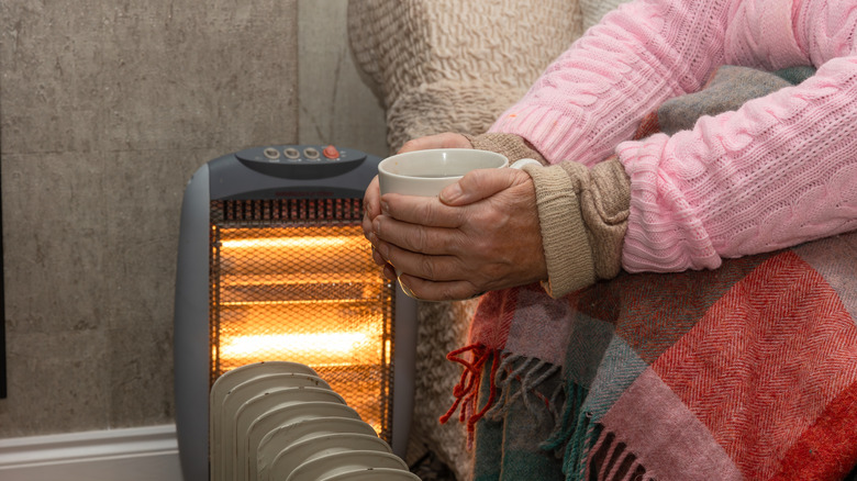 lady keeping warm during cold spell with a cup of tea and an electric heater
