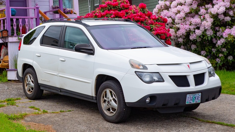 A white Pontiac Aztec parked in the front lawn of a suburban home
