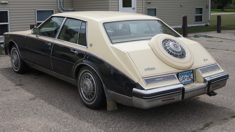 cream and black cadillac seville parked outside pre-fab house