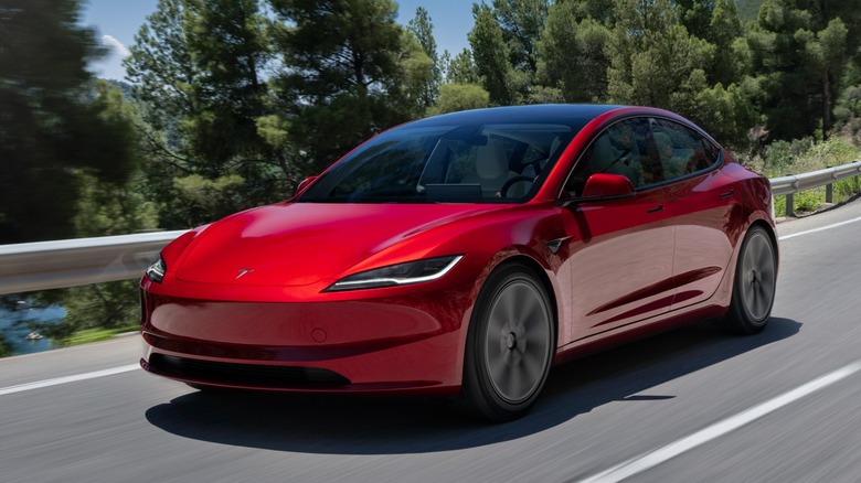 a red Tesla Model 3 driving on a road