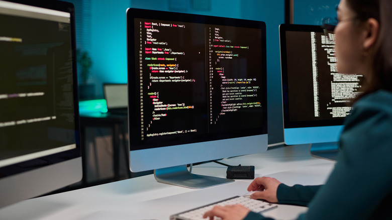 Woman sitting in front of computer screens displaying lines of code