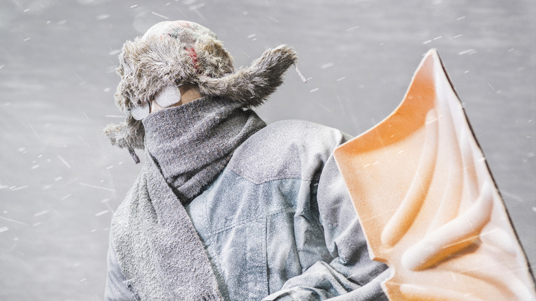 Person in fur hat and goggles shoveling snow in storm