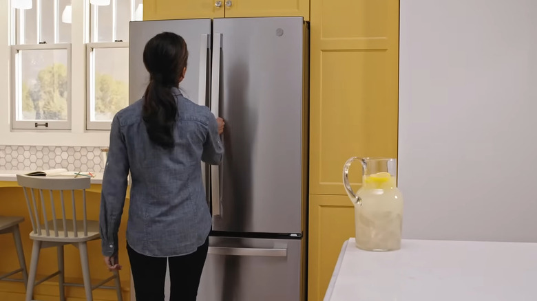 Woman opening GE GNE25JYKFS fridge installed in yellow kitchen