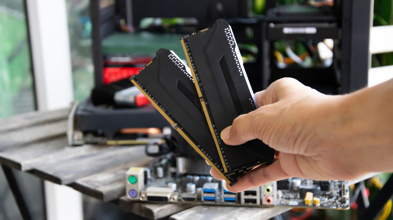 A hand holding two sticks of RAM, motherboard in the background