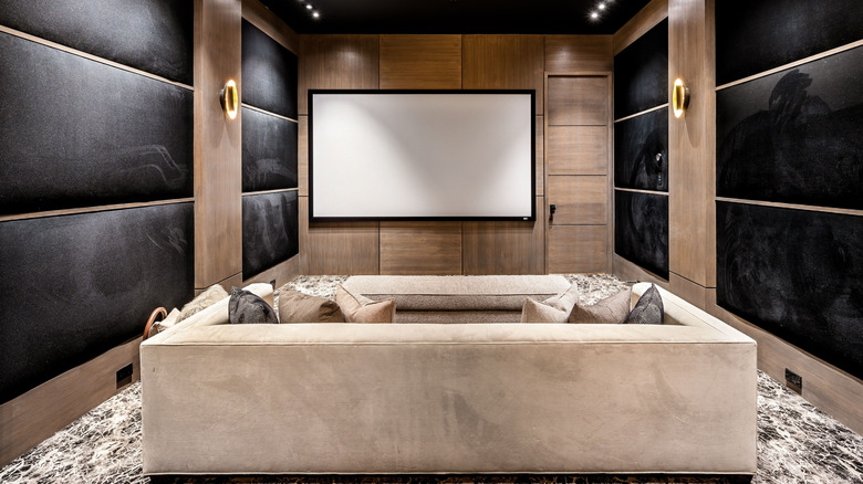 Home theater room with projector screen, sofa, and wooden walls.