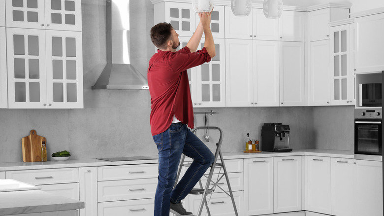 A person using a step ladder to change a lightbulb.
