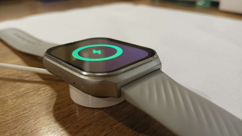 An Apple Watch with a gray band laying on a charger