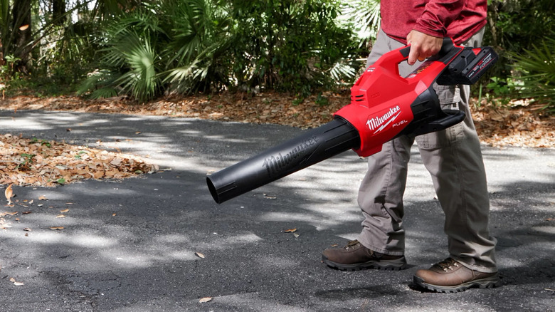 man using a Milwaukee M18 dual-battery leaf blower on street