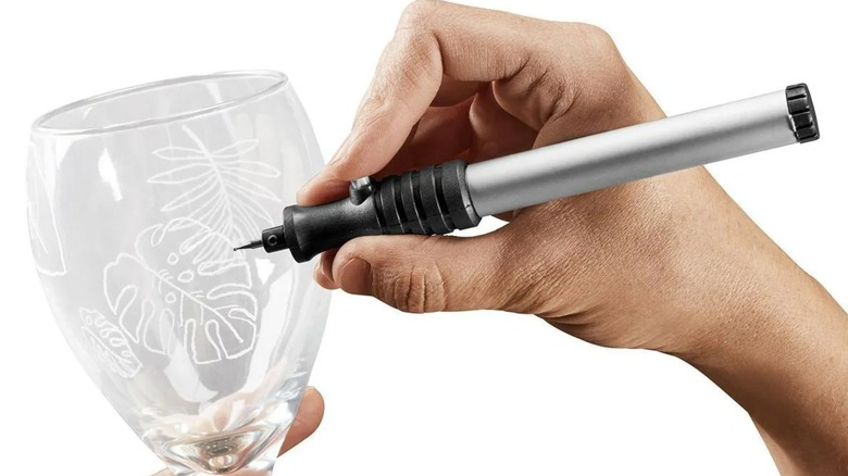 A person using a Warrior engraver on a glass