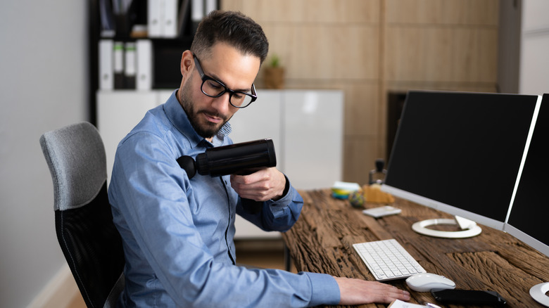 Man at desk using massage gun on shoulder