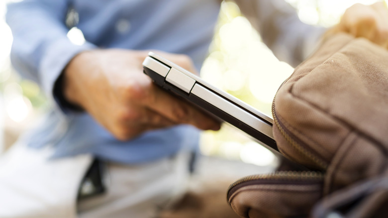 Hands of a young man putting away a laptop in a bag