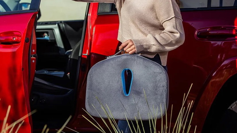a woman holding a Type S Deluxe Memory Foam Seat Cushion getting into her vehicle