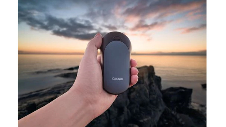 Ocoopa Rechargeable Hand Warmers held up to sunset on rocky shoreline