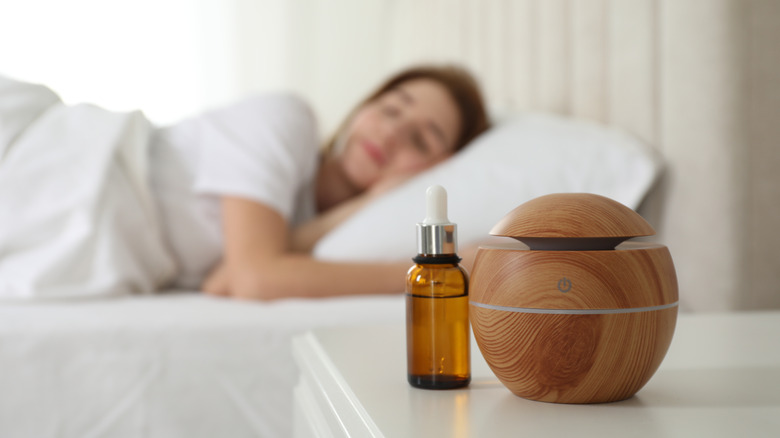 Blurred woman in white bed with an aromatherapy diffuser in focus