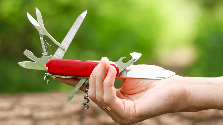 A red Swiss Army Knife held din the hand of someone, with all tools out, with an outdoor background