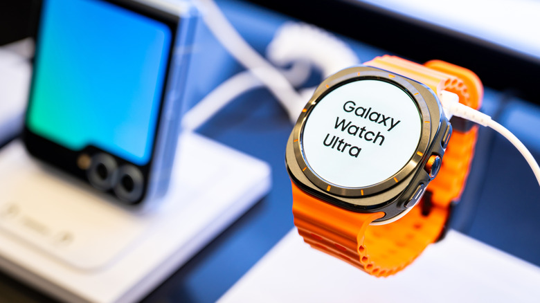 A Galaxy Watch with an orange strap on display next to a flip phone