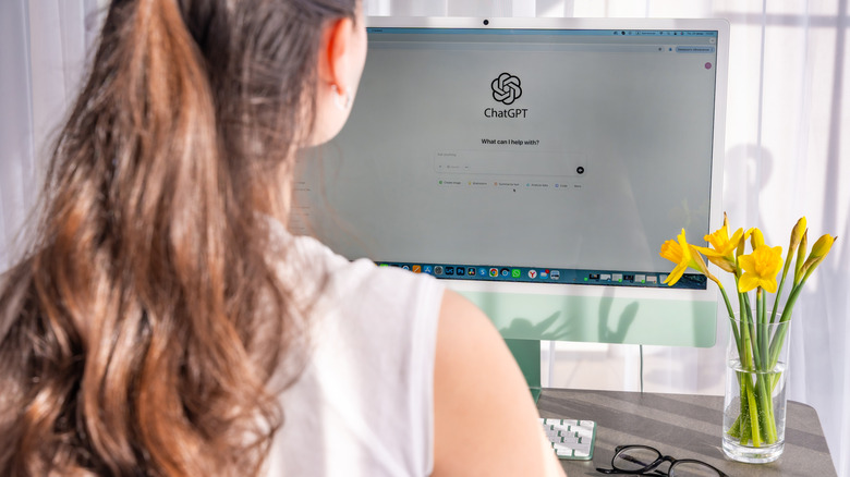 Back view of woman working on iMac with ChatGPT application on screen.