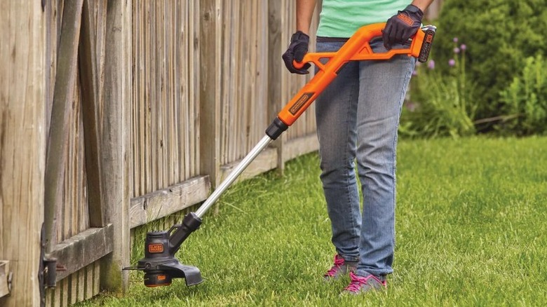 Person trimming grass with Black and Decker string trimmer