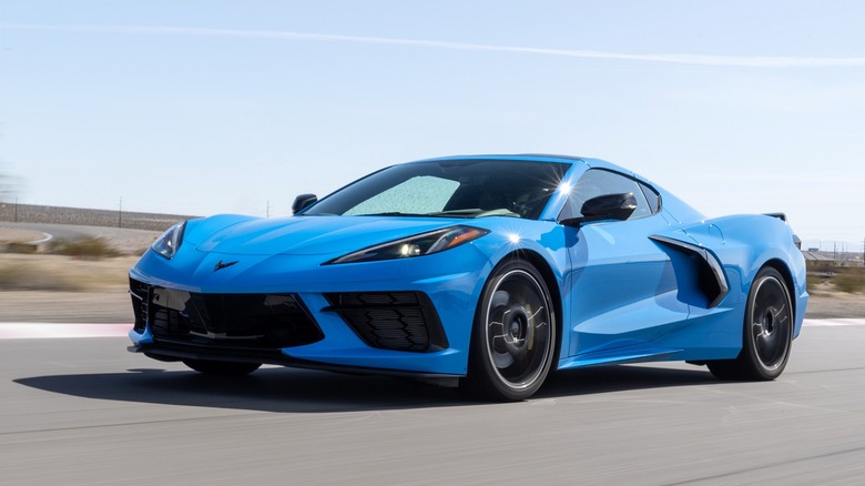 A blue 2020 Chevrolet Corvette C8 Stingray ripping down a drag strip under a clear blue sky.