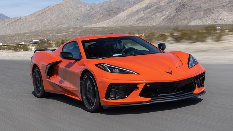 A bright orange 2020 Chevrolet Corvette Stingray driving at speed through a mountainous desert landscape.