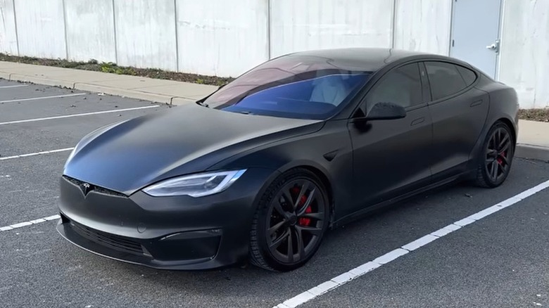 A black Tesla Model S Plaid sitting in a parking lot, framed by a plain concrete wall.