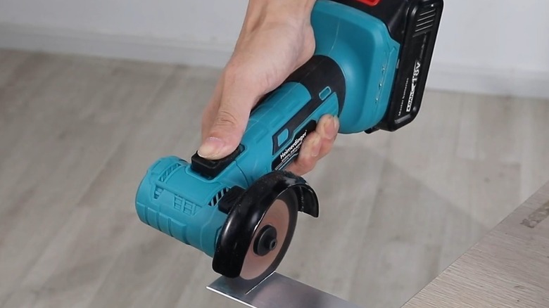 Teal and black angle grinder cutting a metal piece