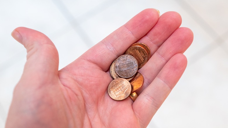 A hand holding some US pennies on a white background