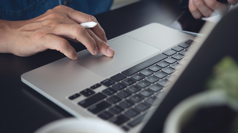 A person working on a laptop at a desk with a pencil in their hand