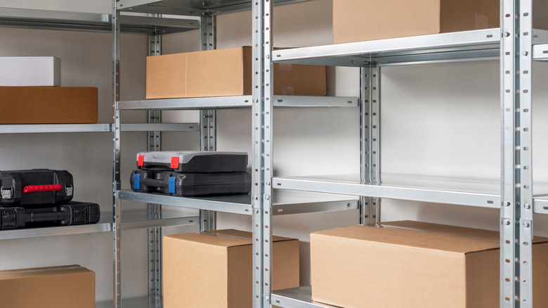 Tall metal shelves with keyhole slots hold cardboard boxes and tool boxes