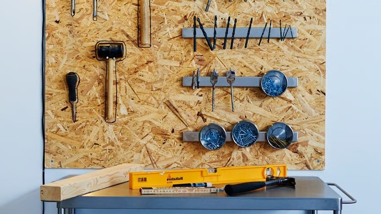 Tools hung on a cork board next to several magnetic knife holders holding drill bits and other items
